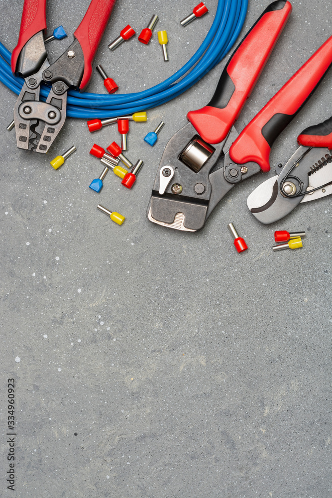 Tools and tips of different sizes and colors for crimping stranded electrical wires. Crimping tools, wire tips and electrical cable on a grey concrete background	
