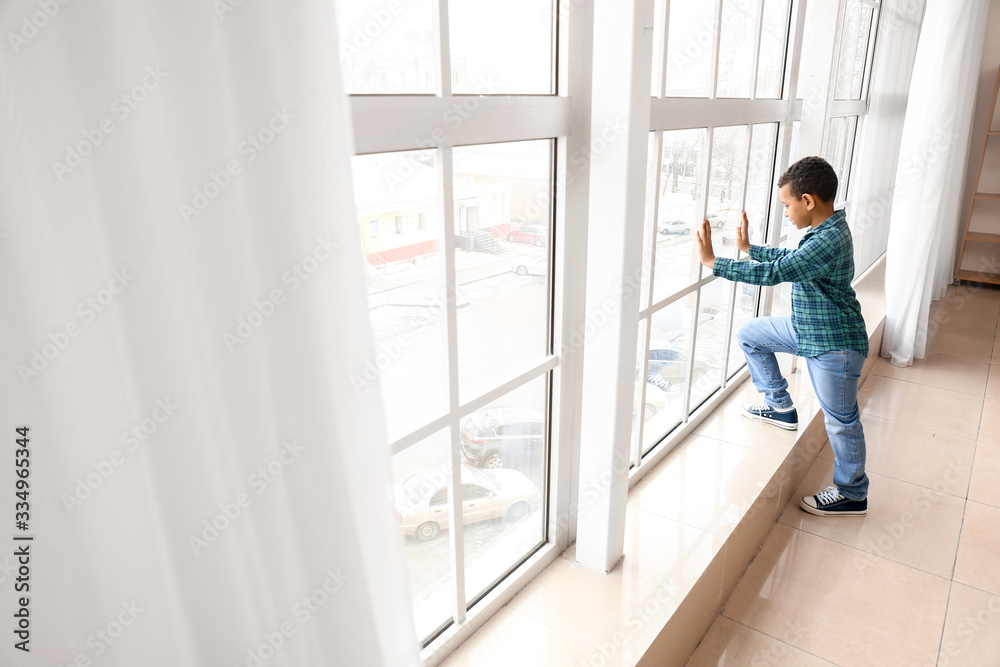 Little African-American boy near window. Child in danger