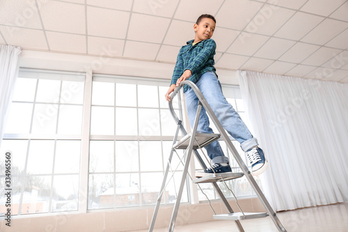 Little African-American boy playing with step ladder at home. Child in danger