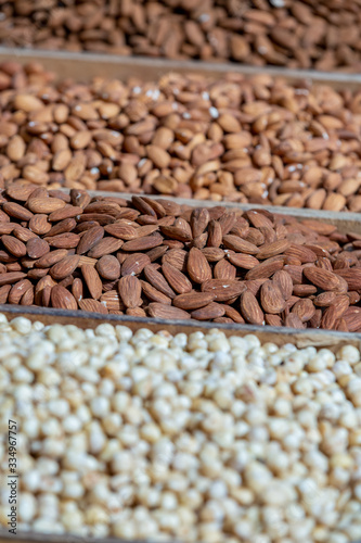 Variety of nuts closeup in tray marketplace, selective focus on almonds, blurred hazelnuts on foreground, blurred peanuts on background