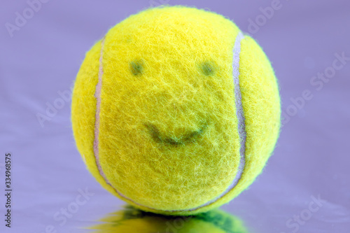 green tennis ball covered with felt and with a smiling face on a purple background