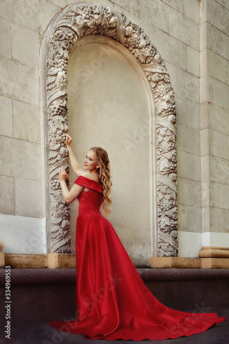 Beautiful blonde girl in a red long dress on a background of architecture, columns 