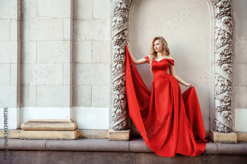Beautiful blonde girl in a red long dress on a background of architecture, columns 