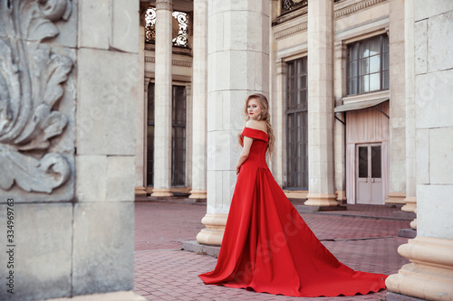Beautiful blonde girl in a red long dress on a background of architecture, columns 