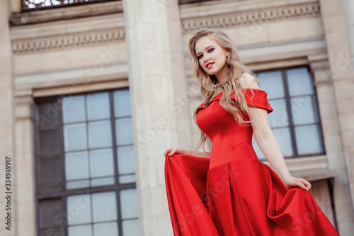 Beautiful blonde girl in a red long dress on a background of architecture, columns 