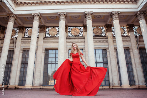 Beautiful blonde girl in a red long dress on a background of architecture, columns 