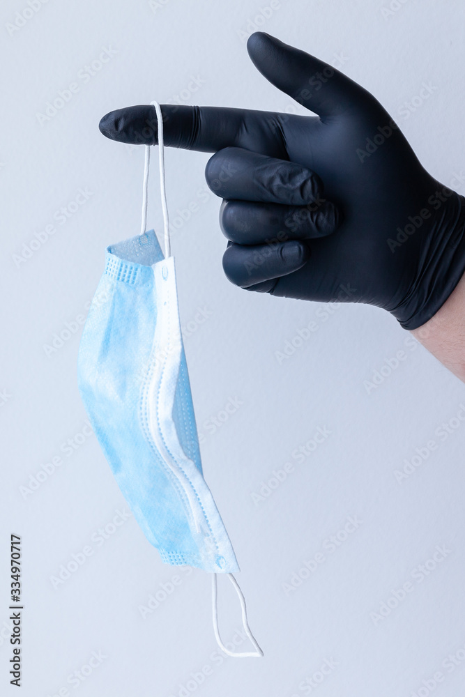 A male hand in medical gloves holds a protective medical mask. Pandemic virus. A male hand in medical gloves holds a protective medical mask. Pandemic virus.