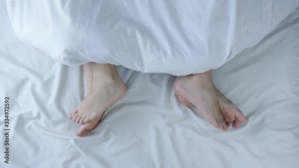 Couples feet sticking out from under duvet at home in bedroom. Feet of a couple sleeping on their opposite sides in bed. Top view. Marriage, family, love, sex concept.