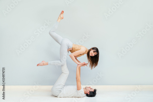 Loving young couple having acro yoga practice in bed at home, sporty strong shirtless man holding slender attractive woman, happy smiling girlfriend doing sport exercise with boyfriend, trust concept photo