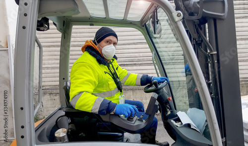 coronavirus : man with protective mask and gloves drives the forklift © Lsantilli