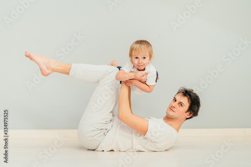 Happy loving father lying on a floor of an apartment, lifting his baby in the air. Smiling, laughing.