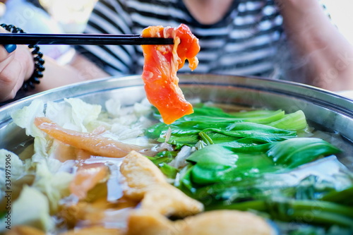 Woman holding sliced beef meat by chopsticks shabu shabu is Korean or Japanese style beef in hot pot dish of thinly sliced meat and vegetables boiled in water. delicious food most popular in thailand. photo