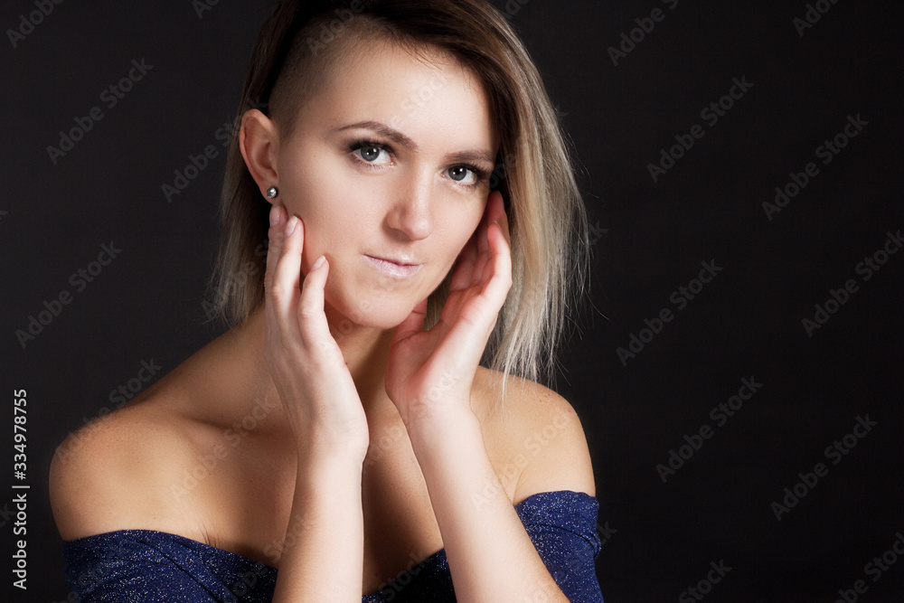 Portrait of a blonde woman in a grey shiny dress on a black studio background. hands at the cheek Portrait of a blonde woman in a grey shiny dress on a black studio background. hands at the cheek