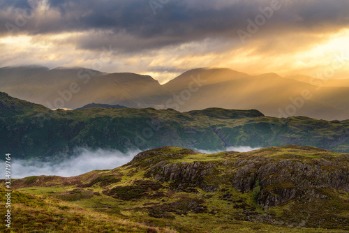 Beautiful Golden Rays Of Sunlight Breaking Through Clouds On A Misty Morning In The English Lake District.
