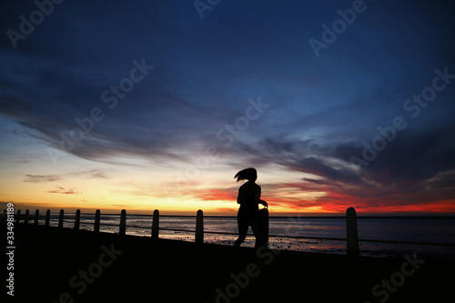 Silhouetted sportswoman training for fitness on seaside promenade at sunset running.