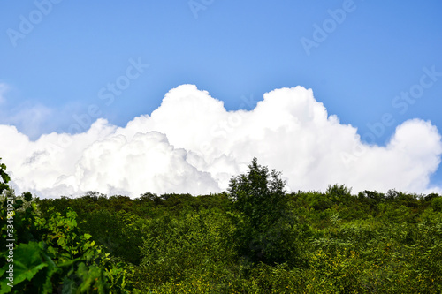 Mountain of white fluffy clouds rises above a green slope against a crystal blue sky.