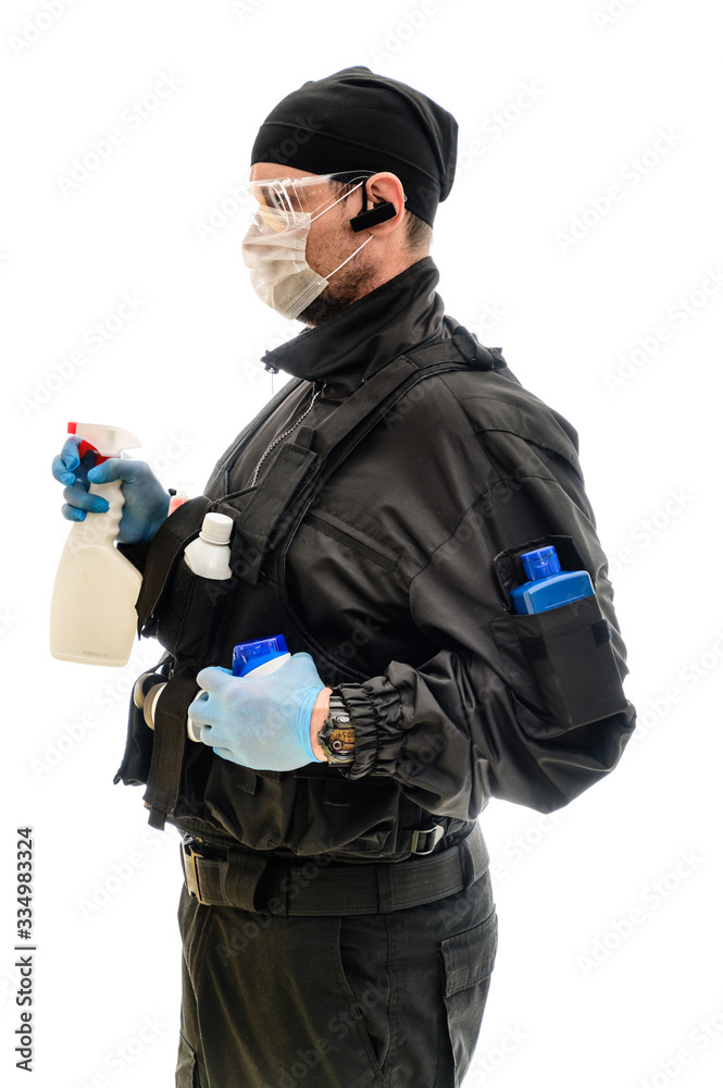 Isolated portrait on white background man in a black military uniform in a medical mask with cleaning products in his hands Isolated portrait on white background man in a black military uniform in a medical mask with cleaning products in his hands