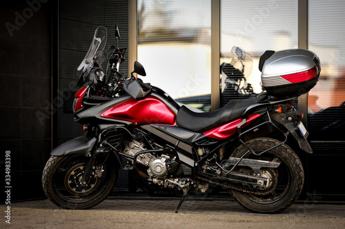 Motorcycle parked in front of office building. Beautiful shiny black motorbike with red details and storage trunk or top box behind the seat. Full length outdoor shot