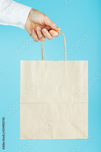 Paper bag at arm's length, brown craft bag for takeaway isolated on blue background. Packaging template layout with space for copying, advertising.