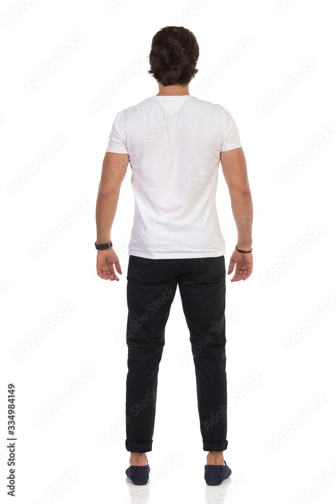 Man In Mocassins, Black Trousers And White T-Shirt Is Standing Relaxed. Rear View. Man In Mocassins, Black Trousers And White T-Shirt Is Standing Relaxed. Rear View.