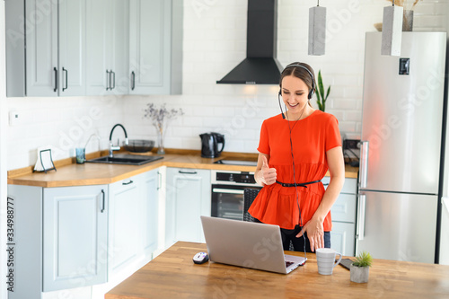 Young woman works from home using headset, laptop