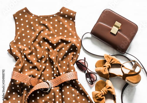 Polka dot brown sleeveless summer dress, cross body bag, sunglasses and suede wedge sandals on a light background, top view. Fashion concept