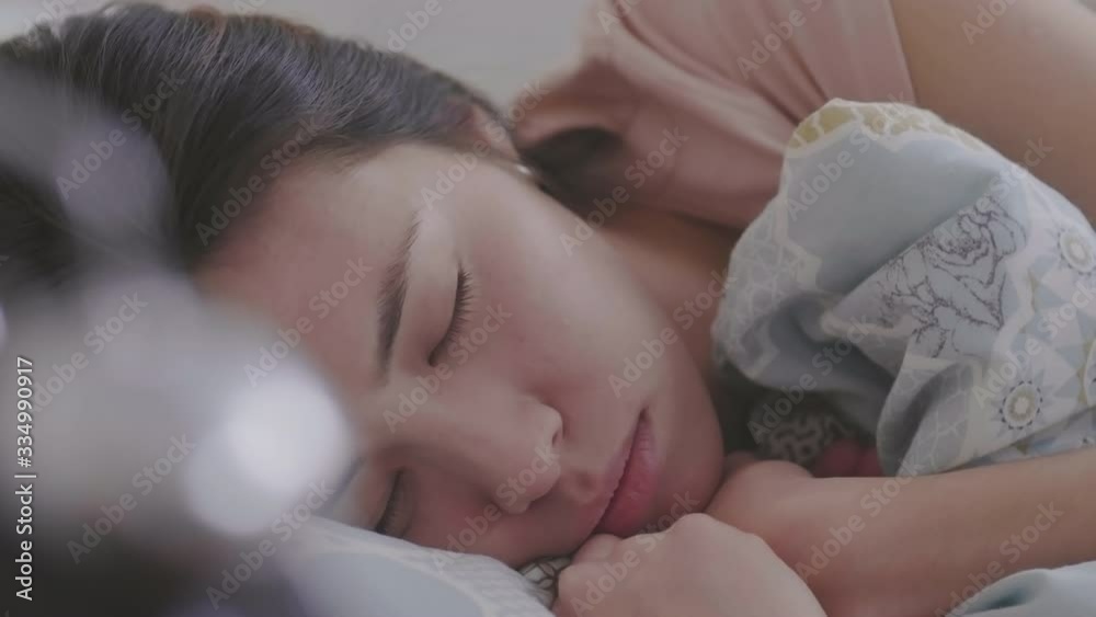 Close up of young sleepy Asian woman sleeping in bed then turning off alarm clock and continuing sleeping Close up of young sleepy Asian woman sleeping in bed then turning off alarm clock and continuing sleeping