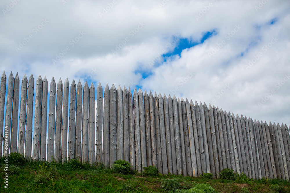 fortress wall of pointed logs against a cloudy sky