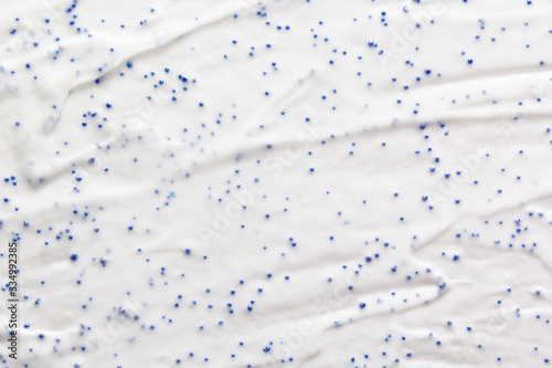 White cream face cleanser scrub texture. Skincare exfoliation cosmetic creamy product with blue particles photo