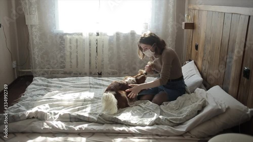 Slow motion of a protective masked young girl with her playing puppy at home during quarantine. Coronavirus. COVID-19 photo