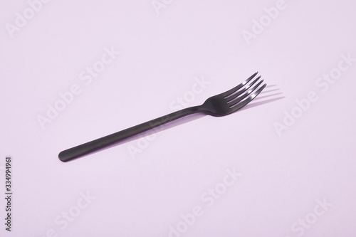 metal shiny black fork on violet background