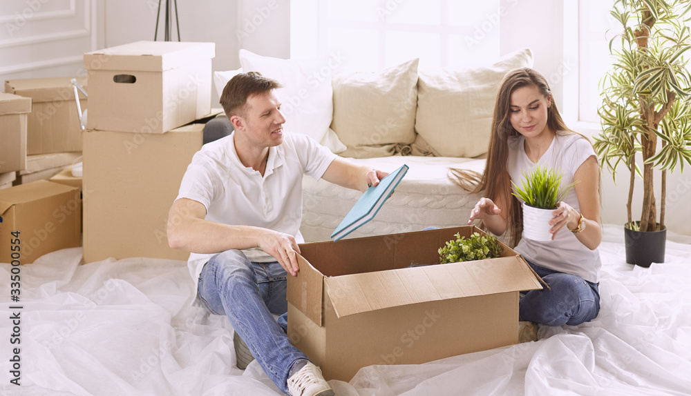 Portrait of happy couple looking at laptop computer together sitting in new house, surrounded with boxes Portrait of happy couple looking at laptop computer together sitting in new house, surrounded with boxes