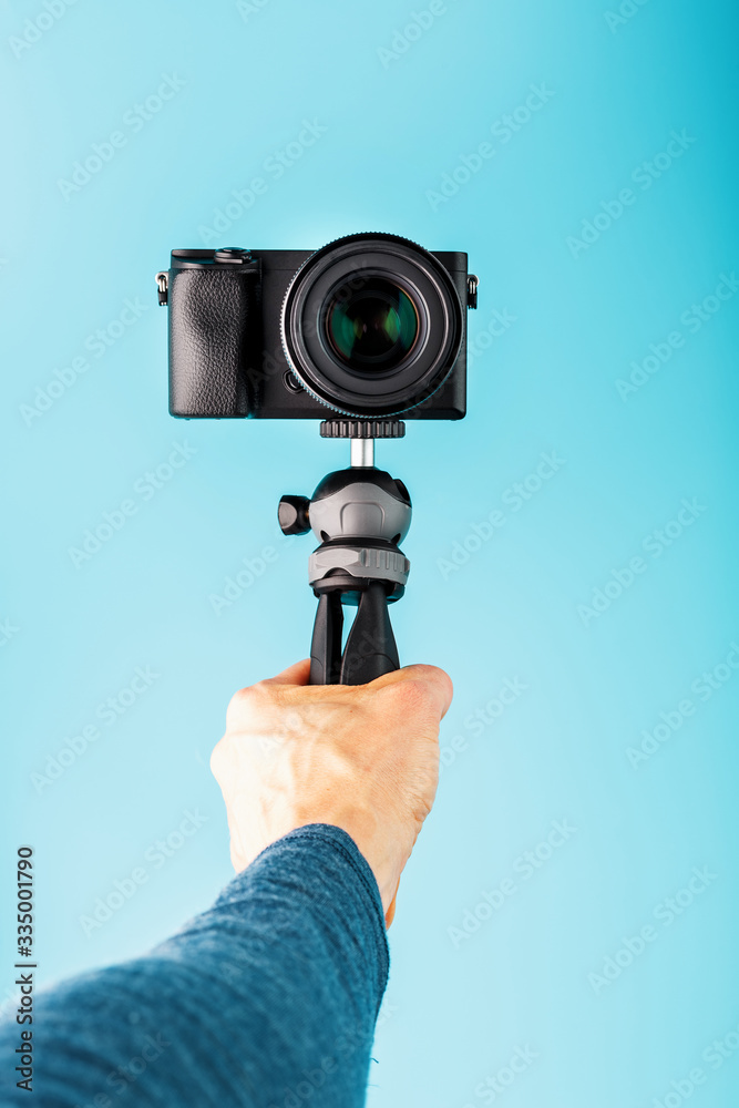 A hand holds a black SLR camera on a tripod, isolated on a blue background.