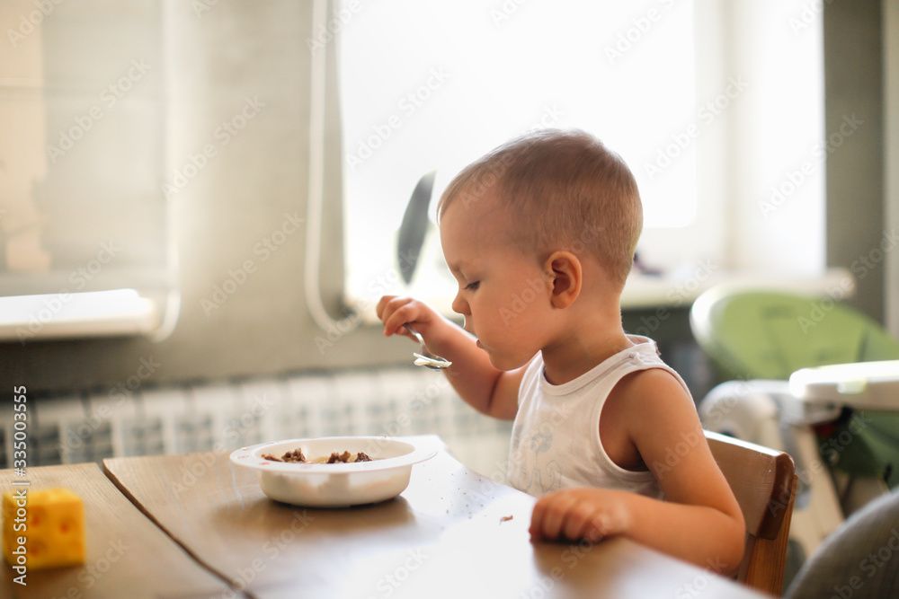 Caucasian boy eats soup at wooden table in kitchen Caucasian boy eats soup at wooden table in kitchen