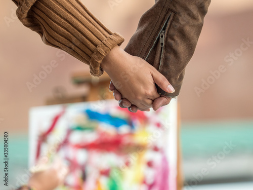 Selective focus on Couple holding hands while looking at artist paint the abstract painting. Valentine, love concept.