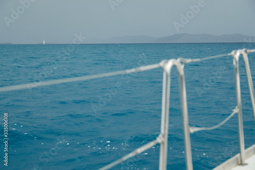 The view of the sea and mountains from the sailboat, edge of a board of the boat, slings and ropes, splashes from under the boat, rainy weather, dramatic sky