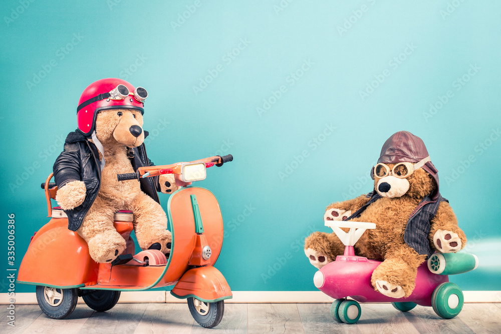 Retro Teddy Bear toy in helmet with goggles on old children's pedal  scooter from 60s and Teddy Bear in leather aviator hat front mint blue background. Kid's race concept. Vintage style filtered photo