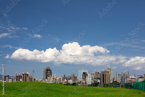 Electric tower on green grass in embankment park, city under blue sky and white clouds