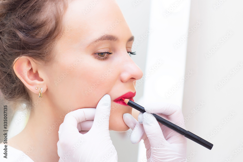 Young woman having permanent makeup on her lips at the beauticians salon. Permanent Makeup (Tattoo). drawing a contour with a white lip pencil Young woman having permanent makeup on her lips at the beauticians salon. Permanent Makeup (Tattoo). drawing a contour with a white lip pencil
