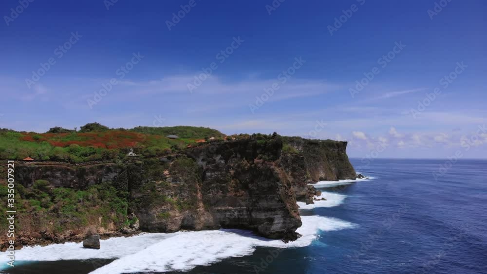 Uluwatu temple on a rock video captured by a drone from the ocean side. The sheer cliffs of the southern coast of Bali are washed by a clear azure ocean. Bukit Peninsula aerial view. Uluwatu temple on a rock video captured by a drone from the ocean side. The sheer cliffs of the southern coast of Bali are washed by a clear azure ocean. Bukit Peninsula aerial view.