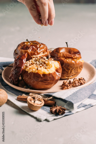 Baked apples with cottage cheese and dried fruits, the hands of the cook pour crushed walnuts, cinnamon on a wooden background. Useful food for diet. Dessert. Side view