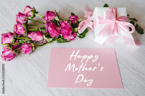 Postcard with bouquet of small pink roses, gift box, on white rustic wooden background. Happy mother's day text sign. Greeting card with flowers concept. Holiday greeting card!