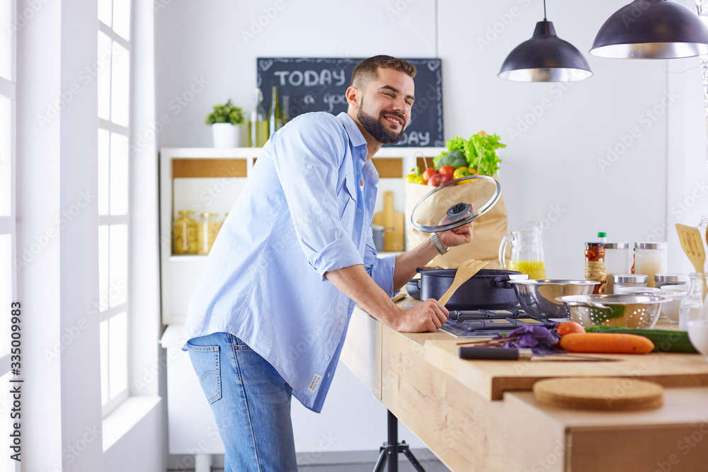 Smiling and confident chef standing in a large kitchen tasting a cooked dish Smiling and confident chef standing in a large kitchen tasting a cooked dish