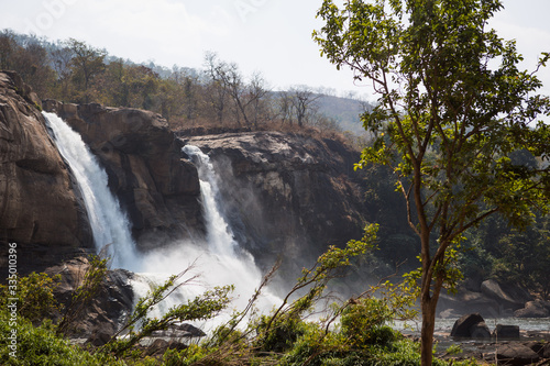 A huge waterfall Athirapally in Kerala  India. White streams of water of the waterfall break into small splashes and flow in a strong stream  Indian tourists look at the attraction