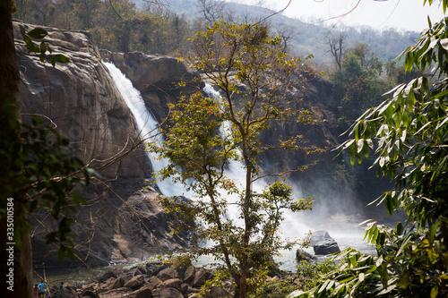 A huge waterfall Athirapally in Kerala, India. White streams of water of the waterfall break into small splashes and flow in a strong stream, Indian tourists look at the attraction