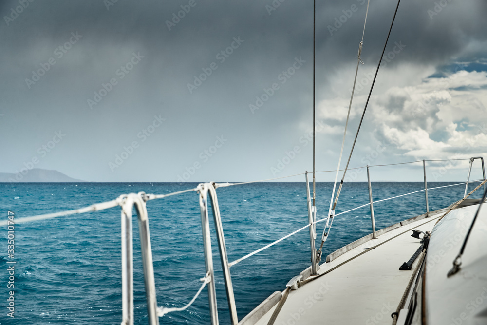 Fototapeta premium The view of the sea and mountains from the sailboat, edge of a board of the boat, slings and ropes, splashes from under the boat, sunny weather, dramatic sky