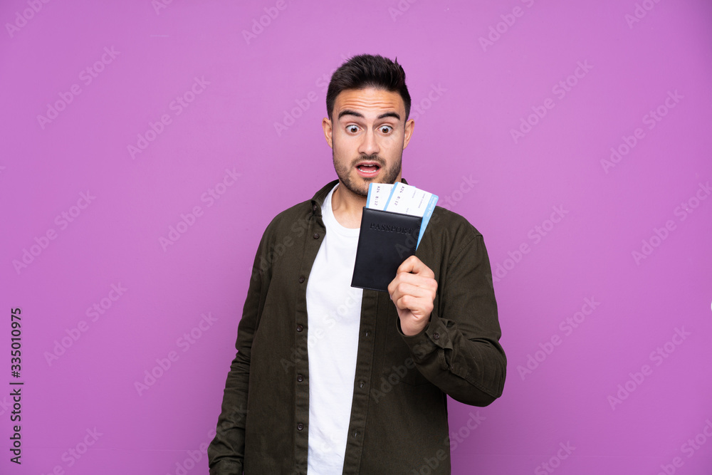 Young handsome man over isolated purple background in vacation with plane tickets and surprised Young handsome man over isolated purple background in vacation with plane tickets and surprised