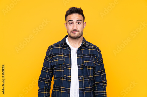 Young handsome man over isolated yellow background having doubts and with confuse face expression