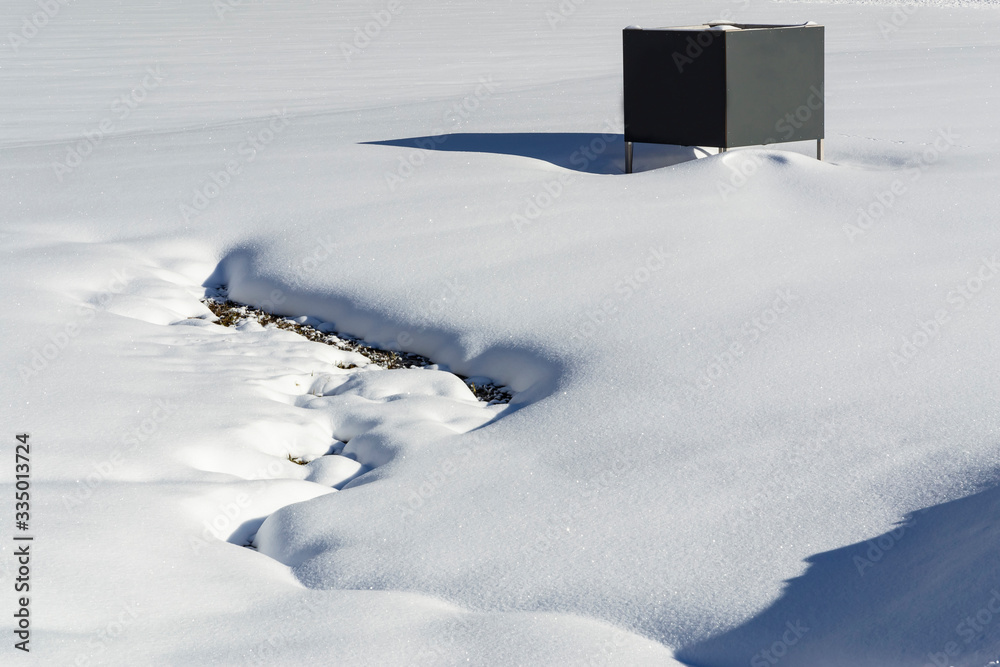 A snowy, winter, countryside landscape of a snow-covered beach of a lake and a gray changing cabin with copy space.