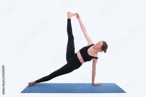 Photo of young sport woman doing yoga on mat over white background in studio